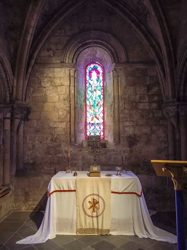 A white cloth covering the altar in the castle chapel. Stained glass window above.