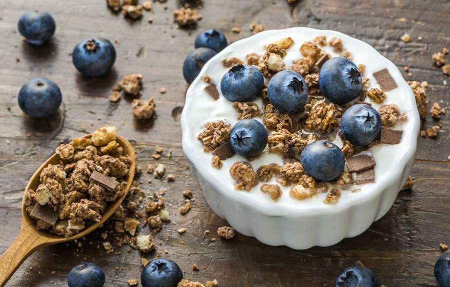 Serving of Yogurt with Whole Fresh Blueberries and Muesli on Old Rustic Wooden Table