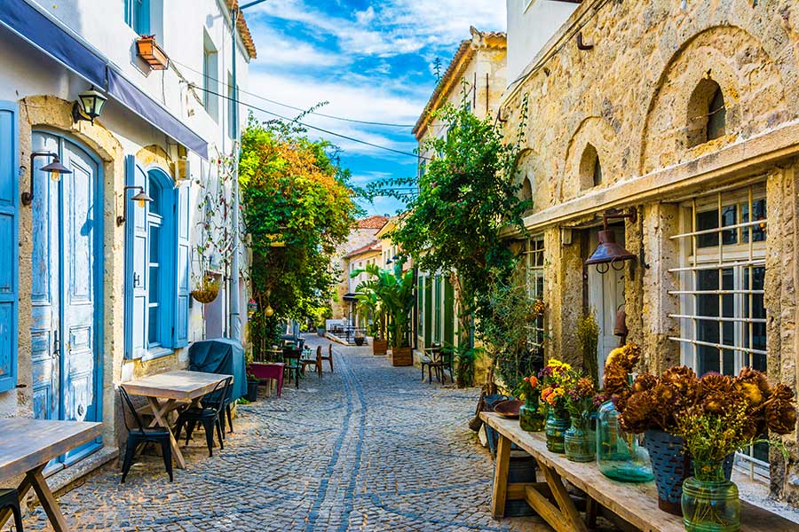 Alacati street view in Alacati Town -Turkey. Tables infront of historical buildings and plants and trees.