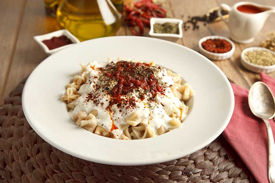 Turkish Manti on plate with red pepper, tomatoes sauce, yogurt and mint