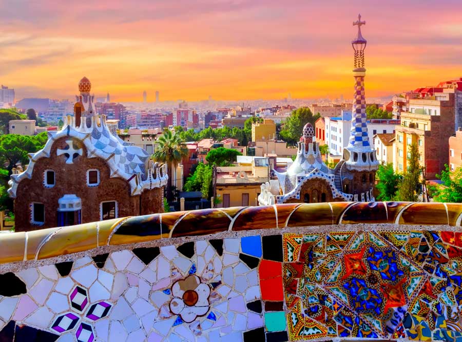 Golden sunrise over the city in the background, with eccentric brightly coloured buildings designed by Gaudi in the foreground.