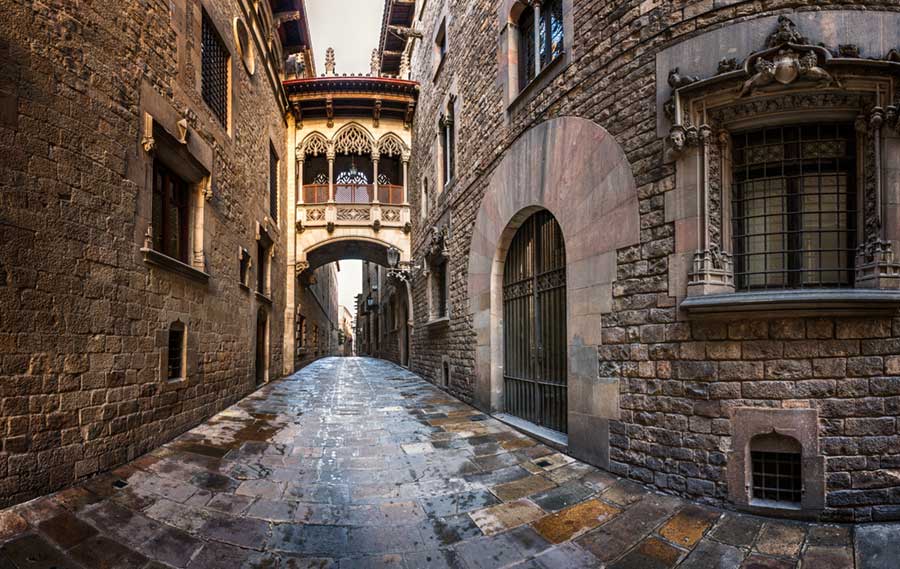 A historic stone alleyway with cobbled streets and a small bridge in the Barri Gotic