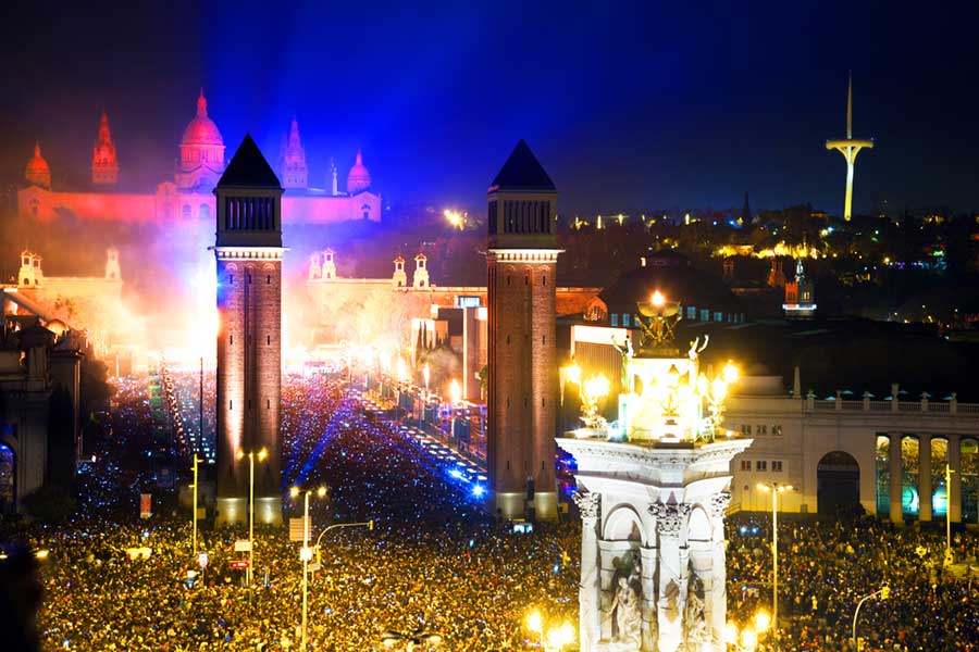 New Year celebrations in the Placa Espana, square full of people with a light show against historic buildings in the background