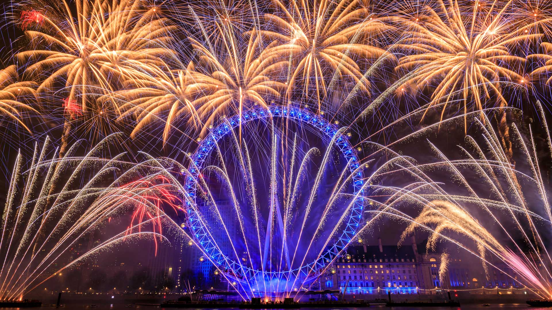 London Eye ferris wheel lit by blue lights with a golden fireworks display surrounding it against the night sky