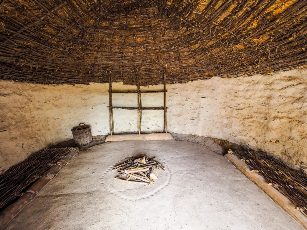 Interior of a neolithic house with stone walls, a central fire and reed seats